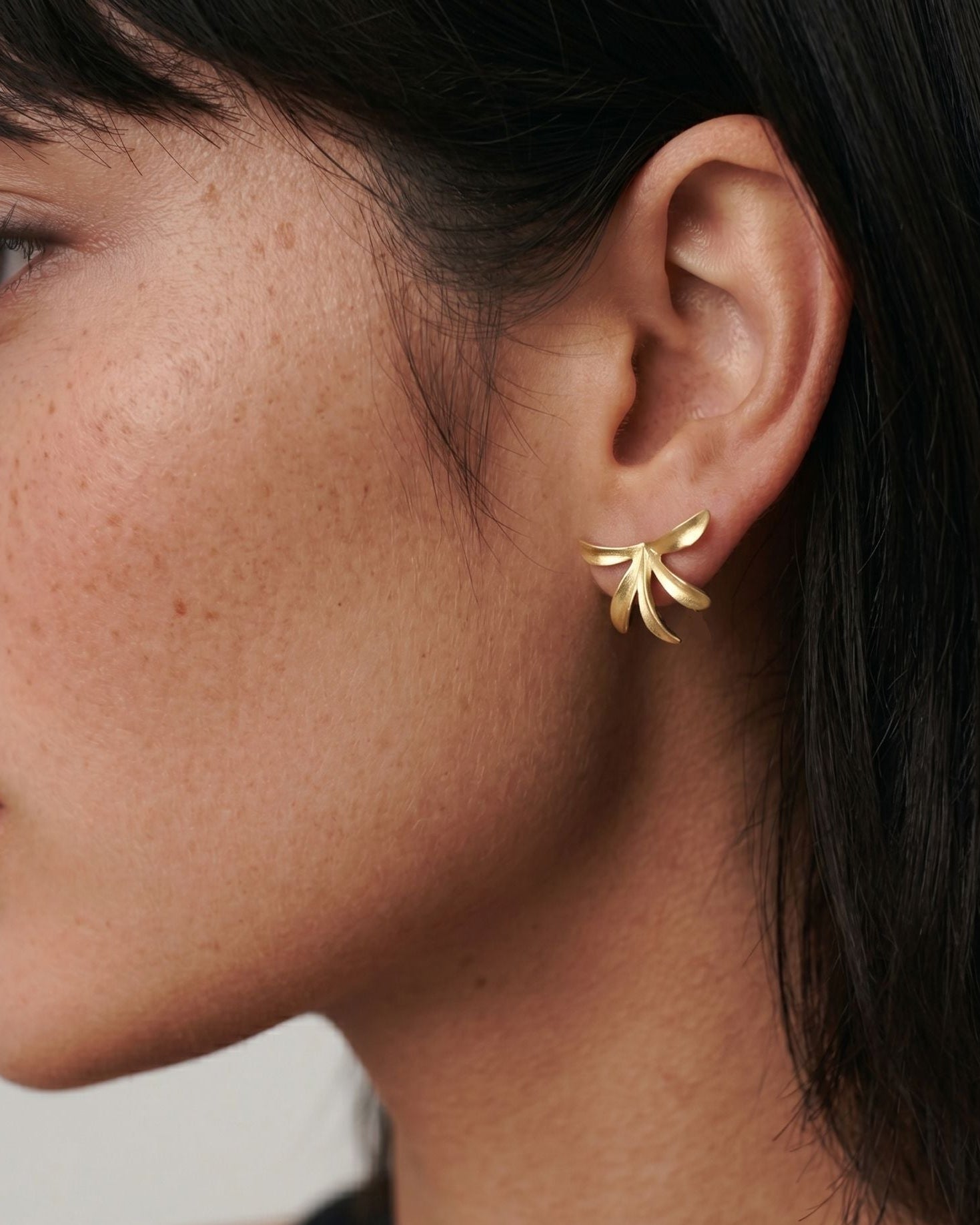 Close-up of a person wearing a gold earring with a blurred background