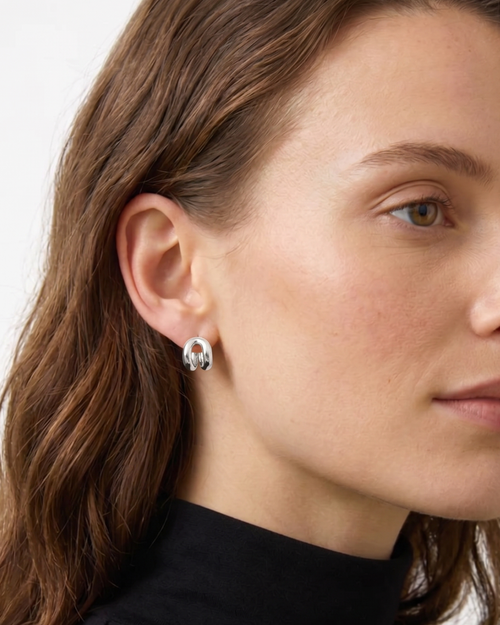 Close-up of a woman wearing silver earrings with a plain background