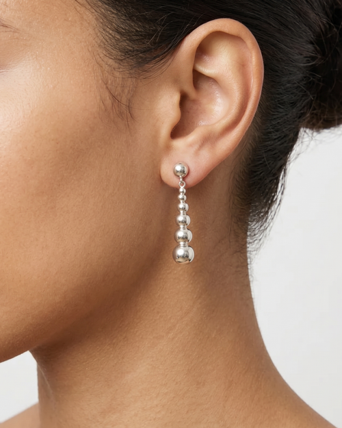 Close-up of an ear wearing a silver earring with a plain background