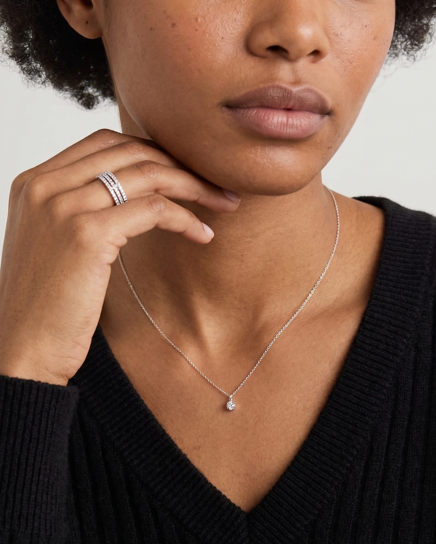 Woman wearing a silver necklace and ring on a plain background
